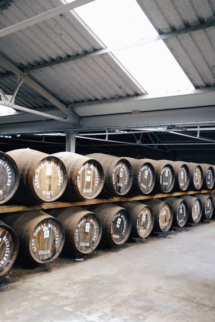 our-mission Neatly stacked wooden barrels in a brightly lit warehouse storage facility.