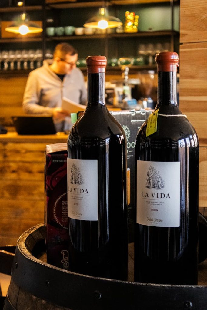 Two wine bottles labeled La Vida on a barrel in a warm, cozy café environment with a blurred background.